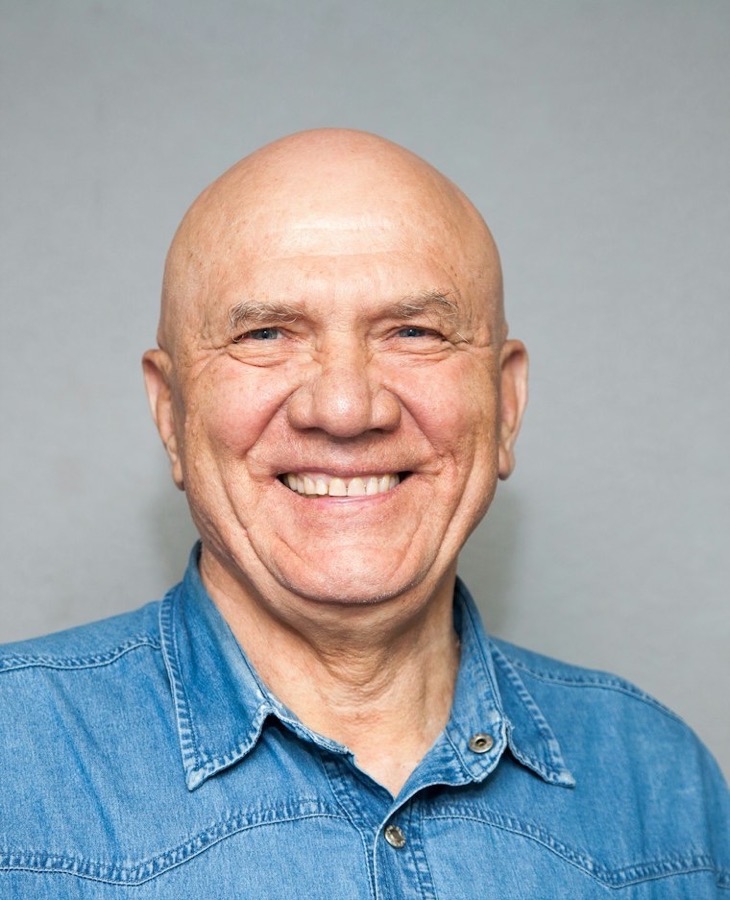 A smiling older man in a denim shirt